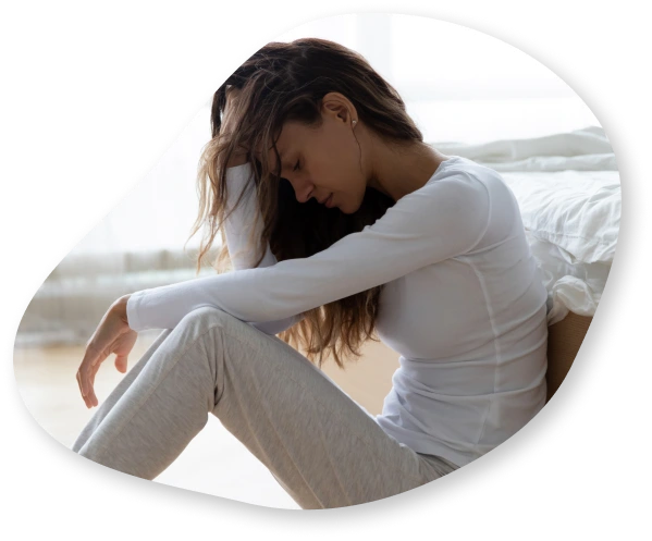 A woman sitting hunched forward with her hand on her head, appearing to be in distress.