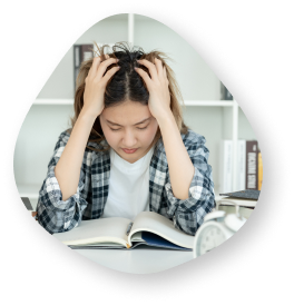 A young woman sitting at a desk, holding her head in her hands and looking stressed while reading a book.