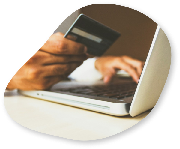 A close-up of a person holding a credit card while using a laptop, representing online payment.