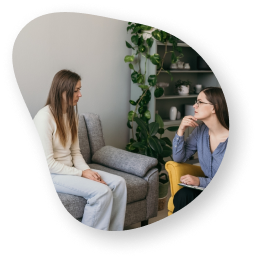 A therapist and a patient sitting in a comfortable, plant-filled room, engaged in a counseling session.