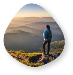 A woman standing on a mountain peak, gazing at the vast landscape of rolling hills and valleys during a sunrise.