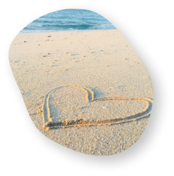 A heart drawn in the sand on a beach with waves gently rolling in the background.