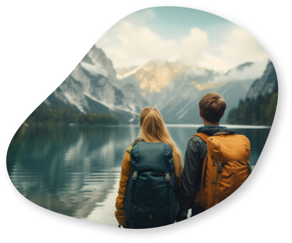 A couple with backpacks standing at the edge of a serene lake, gazing at majestic mountains in the background.