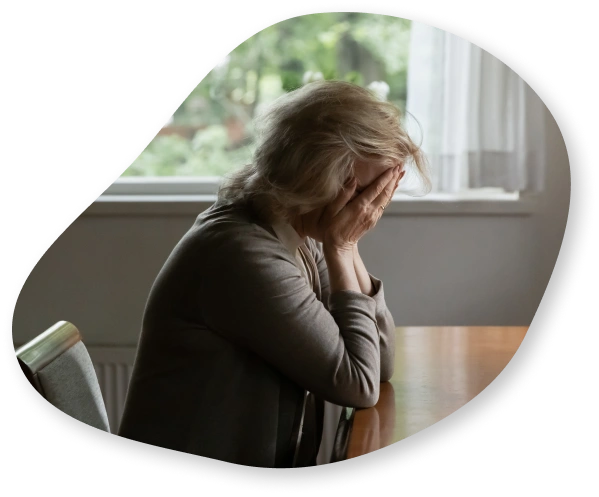 A woman sitting at a table with her hands covering her face, expressing feelings of grief and despair.