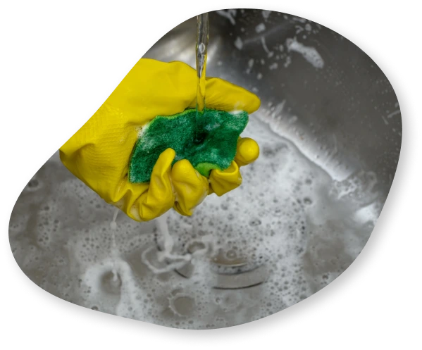 A close-up of a rubber glove holding a sponge underneath running water in a kitchen sink.